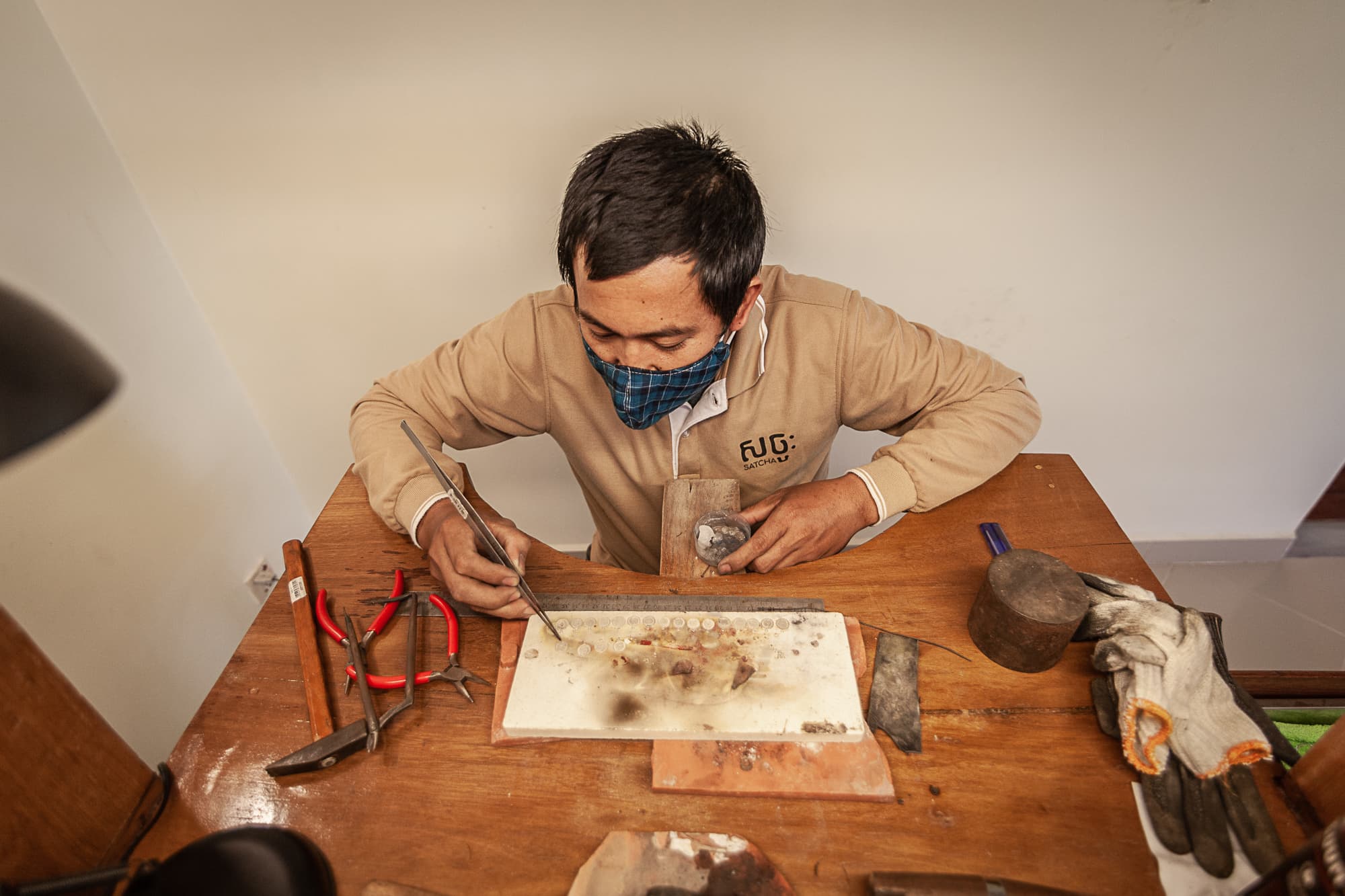 A jeweller working metal at the bench with files and pliers.