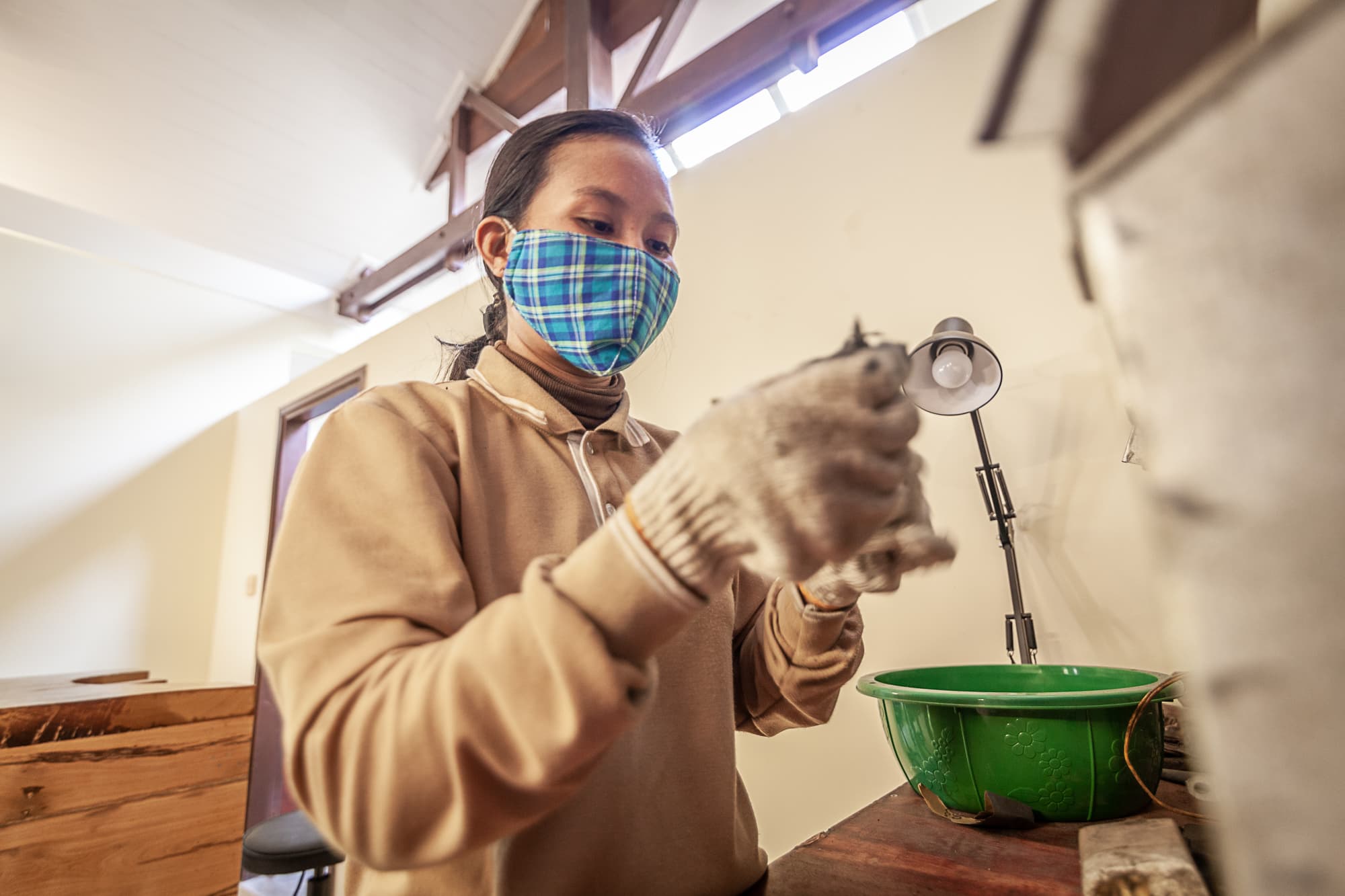 An artisan finishing a silver-plated piece with gloves and lamp.