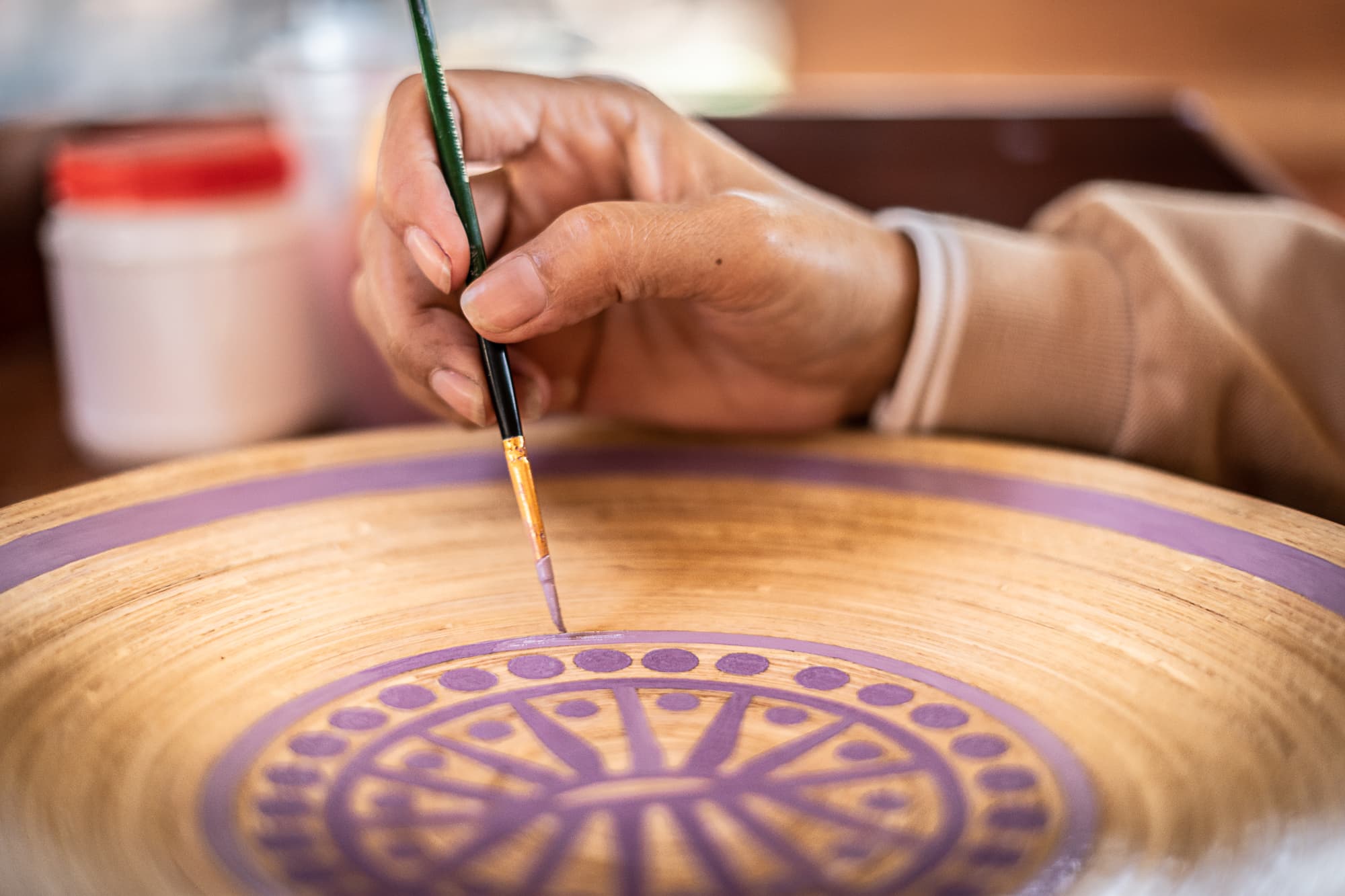 Close-up of an artisan hand-painting a Khmer motif onto a bamboo plate.